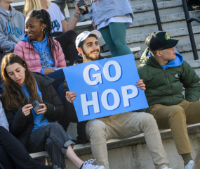 Person sitting in bleachers holding a sign that says "Go Hop"