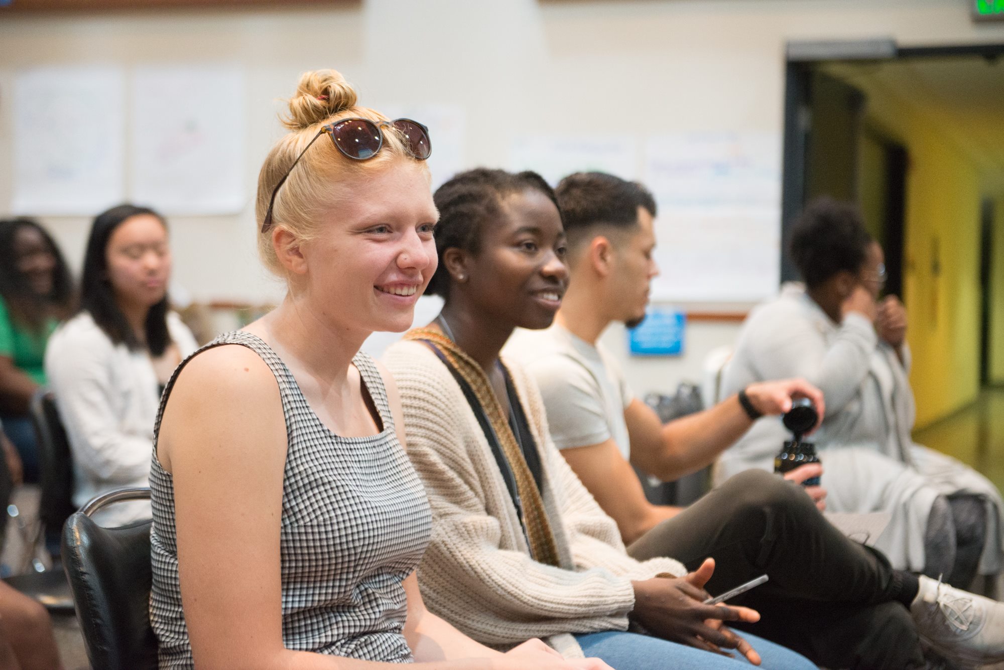 Photograph shows students sitting in a row smiling and looking at someone in the distance.