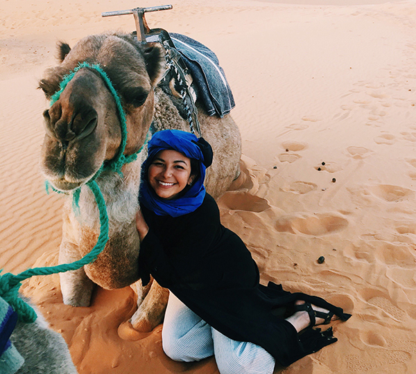 Person poses with a camel in the desert. 