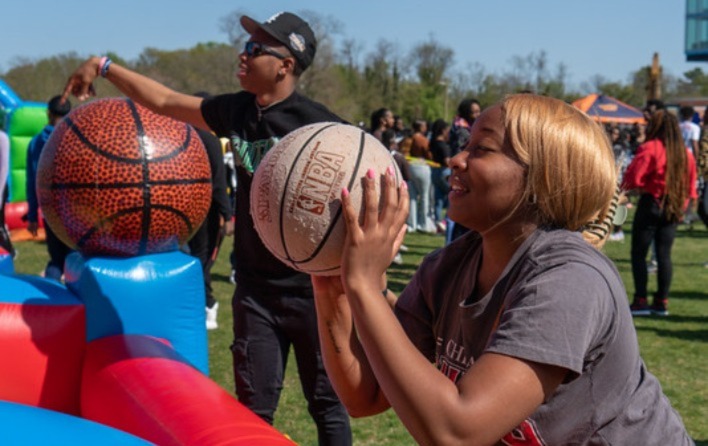 Two people stand with basketballs in hands about to shoot ball at outdoor carnival came. 