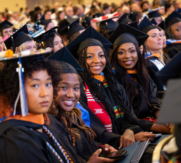 Graduates pose for a photo while sitting at graduation. 