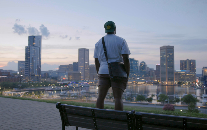 Person stands on bench overlooking Baltimore skyline