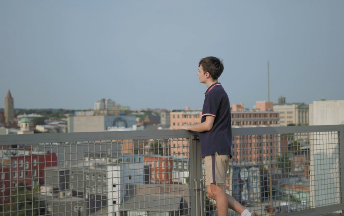Person stands at railing overlooking city.