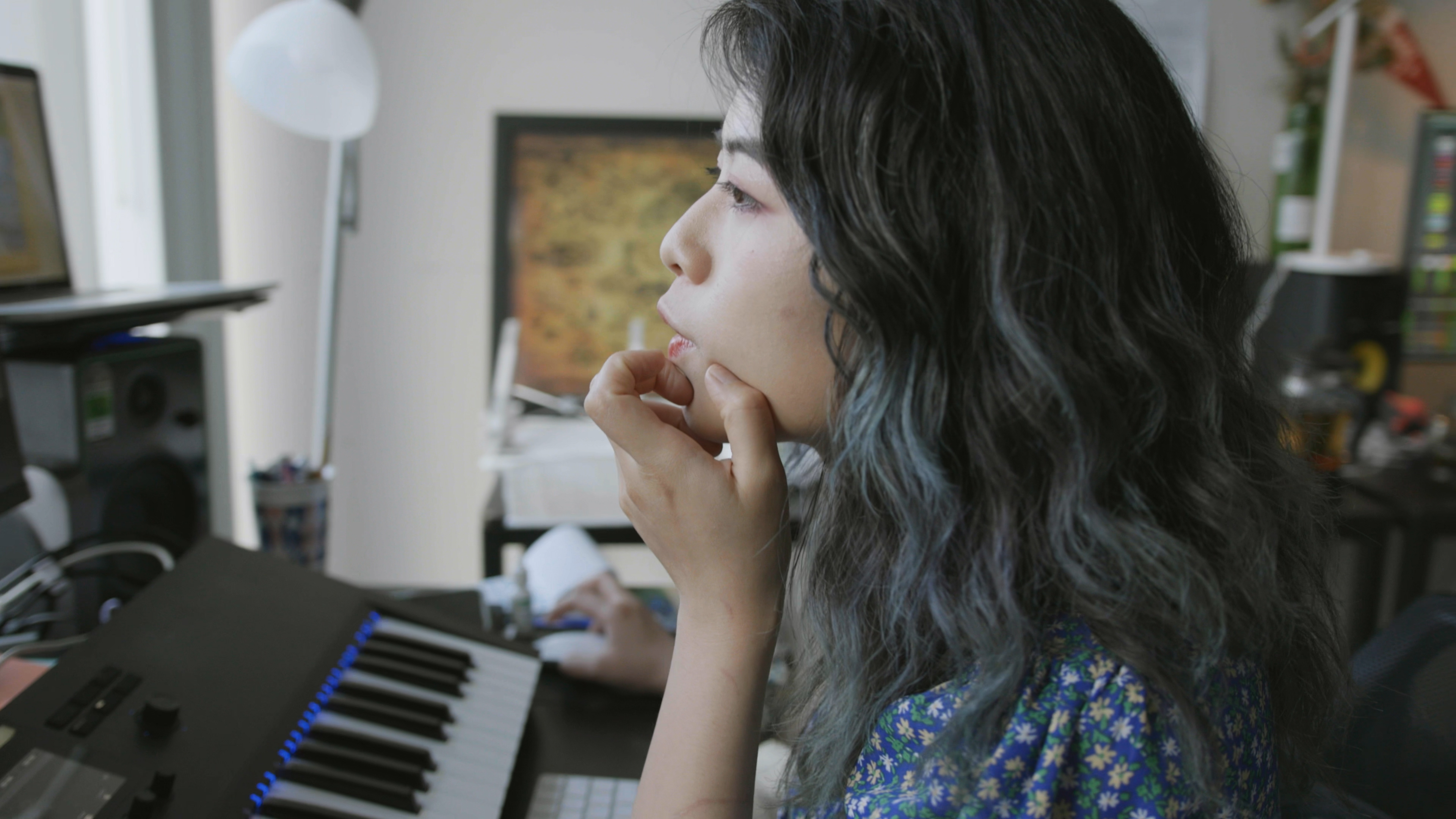 Side view of person sitting at a desk looking at a computer screen with a piano keyboard in front of them.