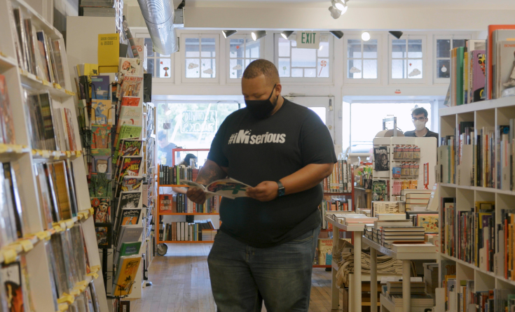 Person stands in comic book store looking at a comic while wearing a face mask.
