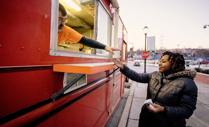 A person grabs a container of food from another person at a food truck window.