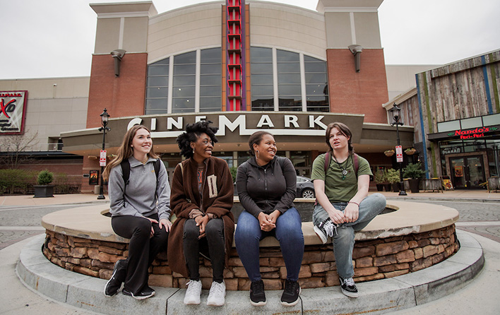 Four people sit on a stone ledge in front of a Cinemark movie theatre.