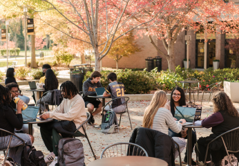 People sit outside at tables on a college campus.