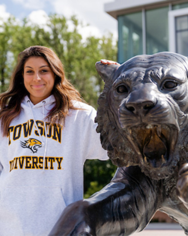 Person in Towson University hoodie stands next to a tiger statue.