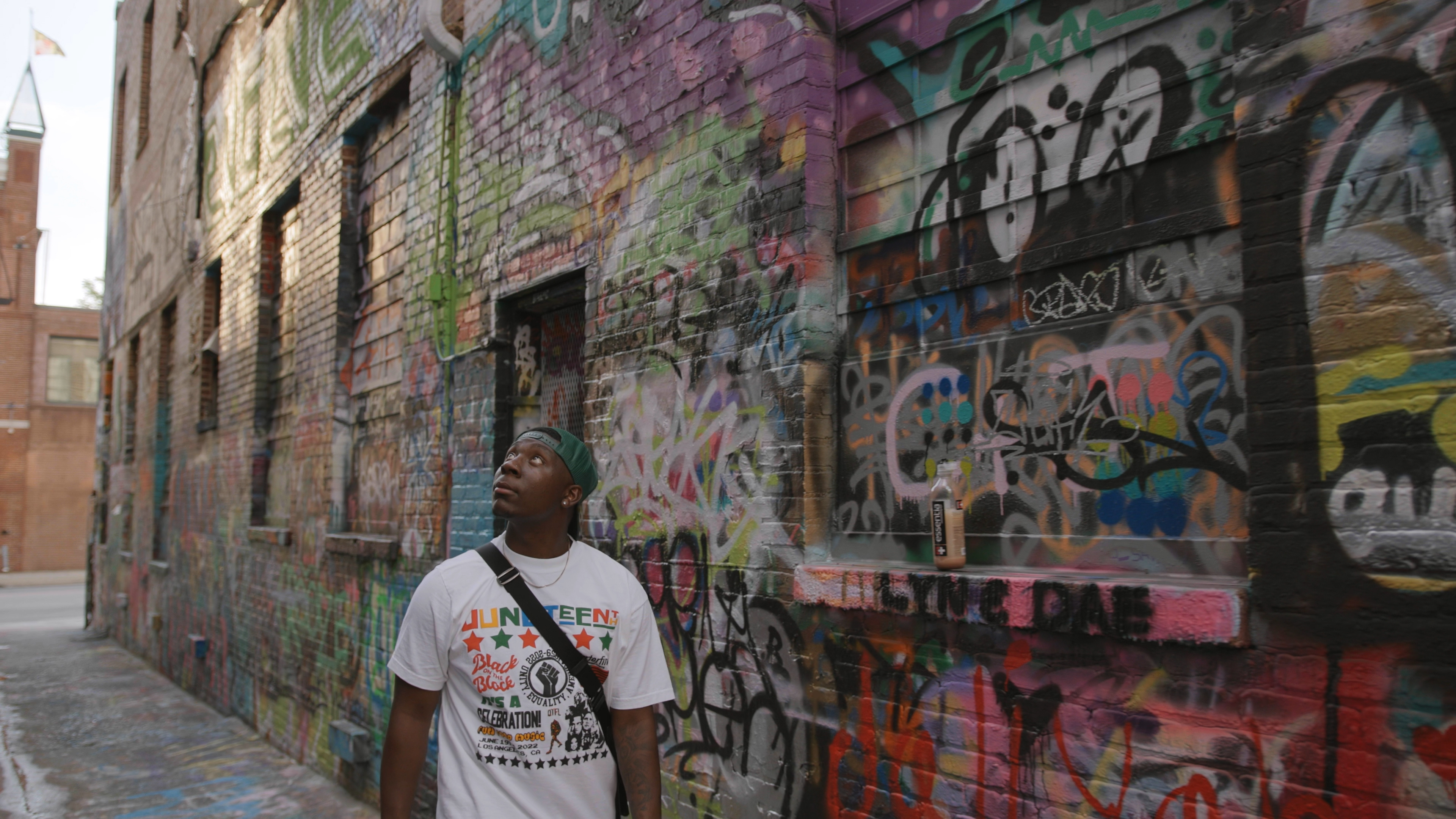 Person looks up at buildings covered with graffiti. 
