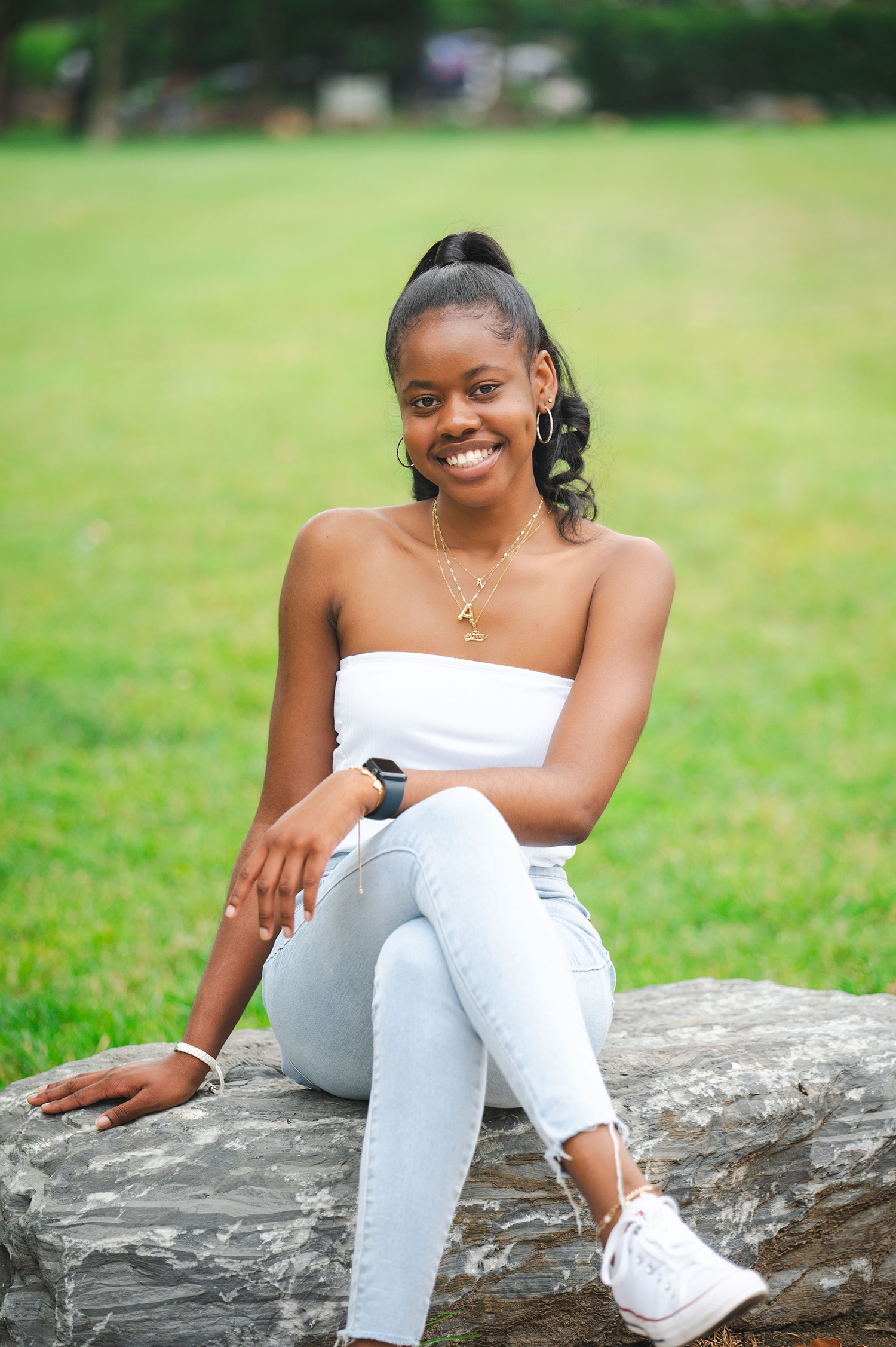 A student smiling while sitting on a rock in a Baltimore park