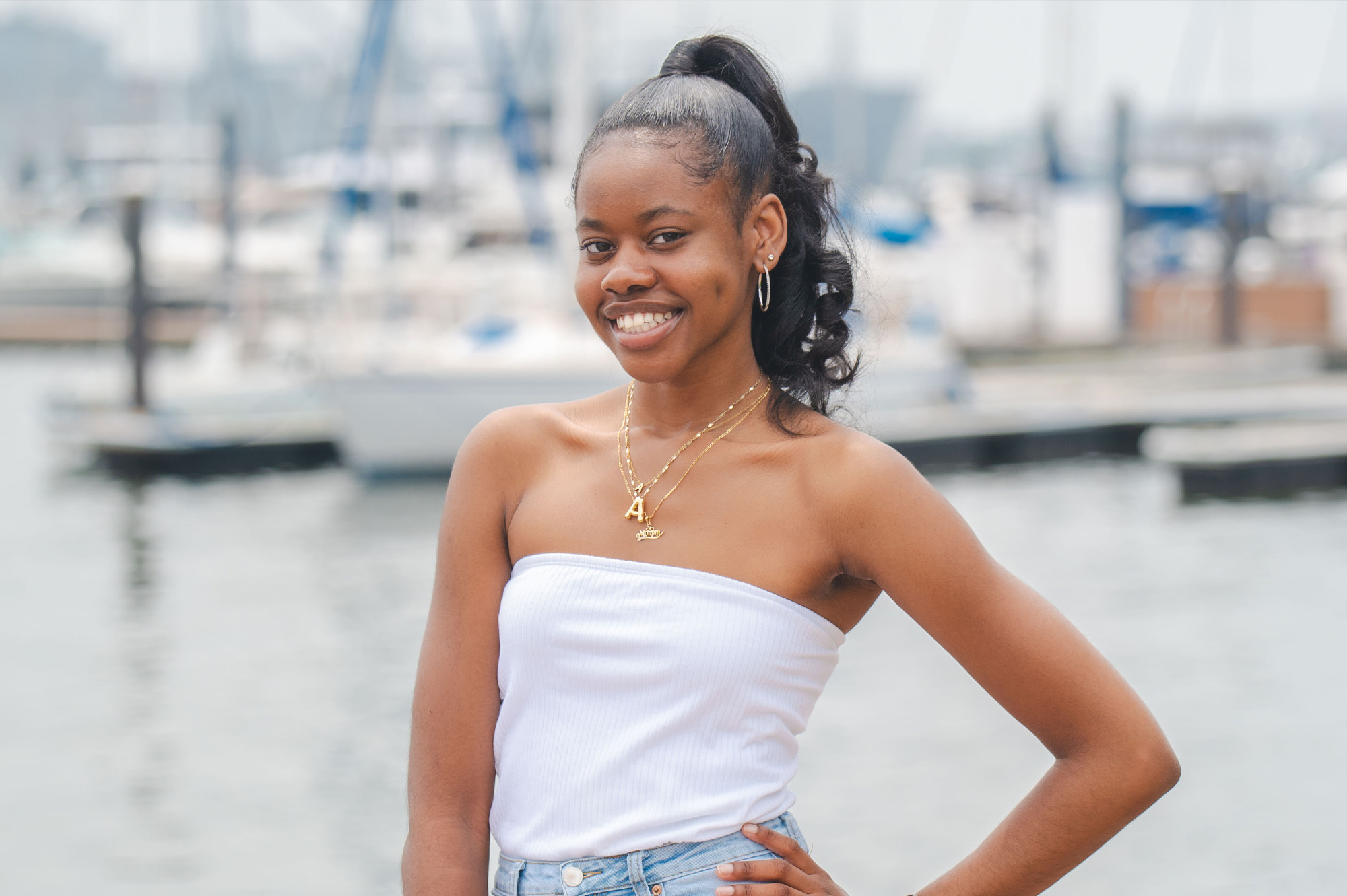 A student poses in front of the Baltimore wharf. Boats are visible on the water in the background.