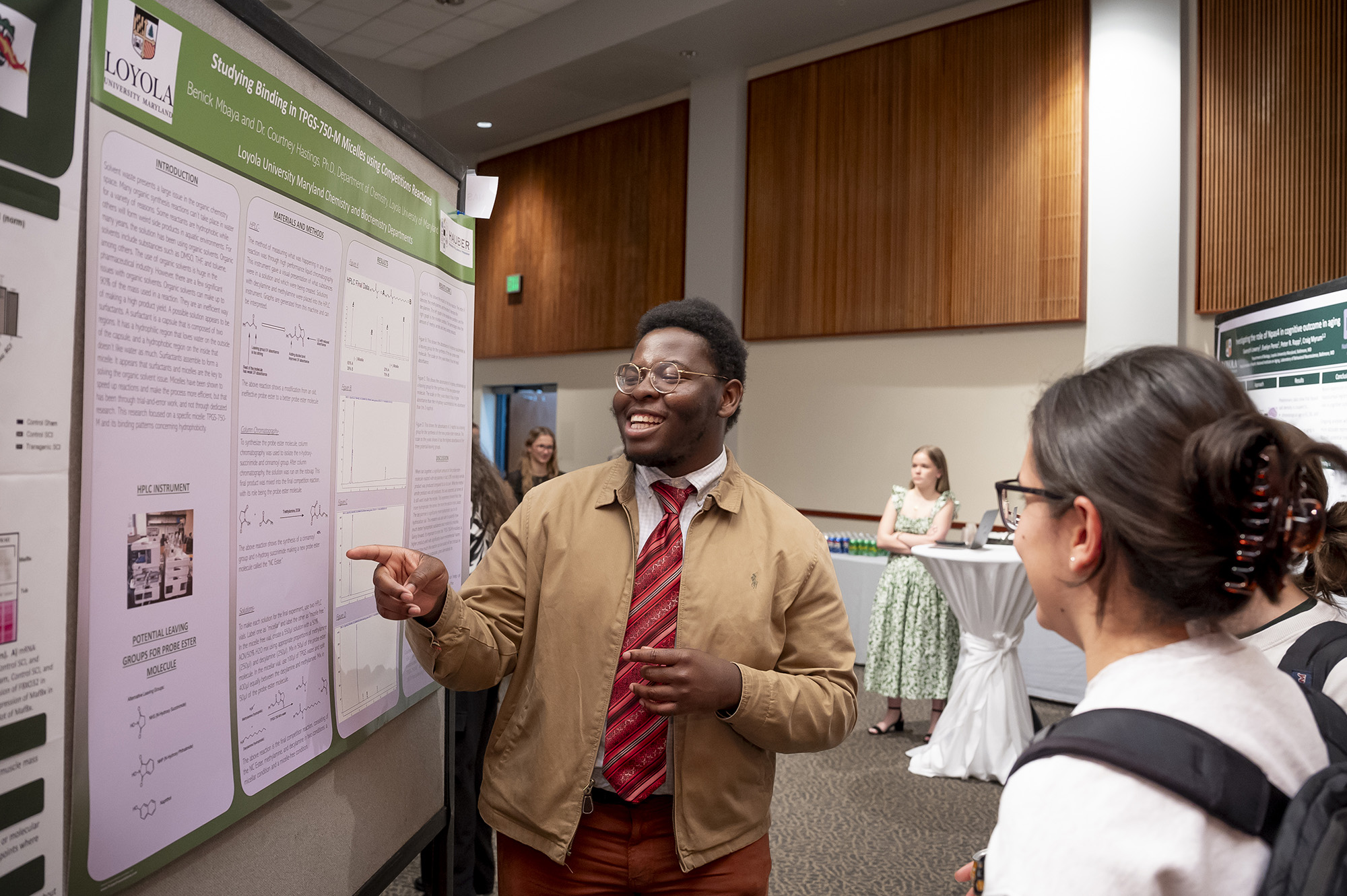 A student gestures to their research project displayed on a poster board.