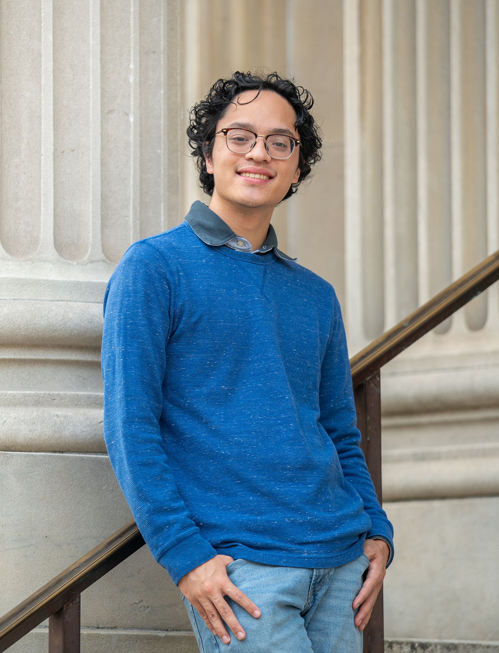 A student poses on a staircase with columns behind.